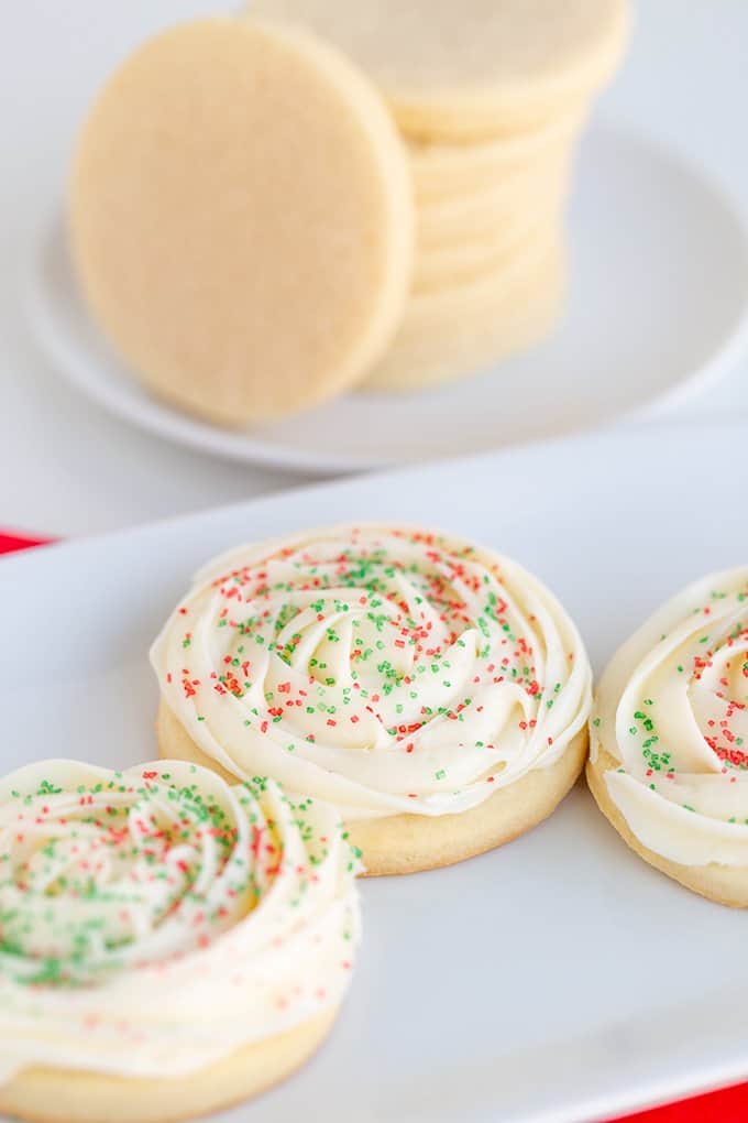 frosted cookies on a white plate with a stack of cookies behind it