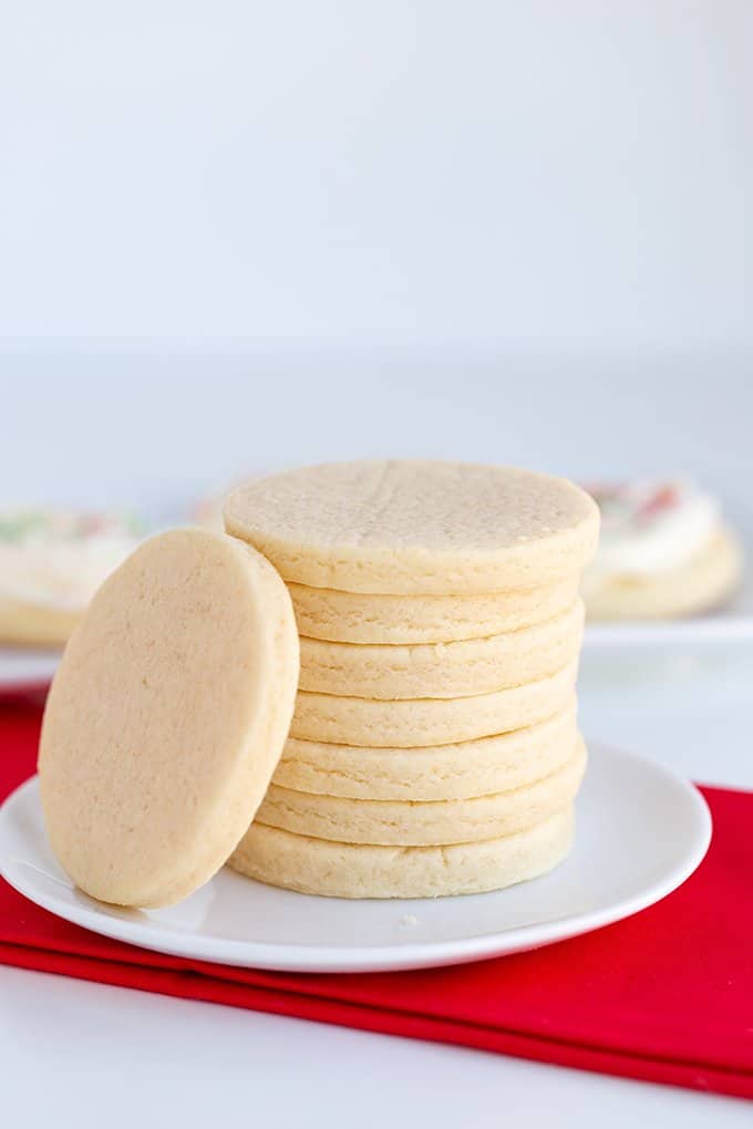 stack of cut out cream cheese cookies on a white plate with a red fabric under the plate