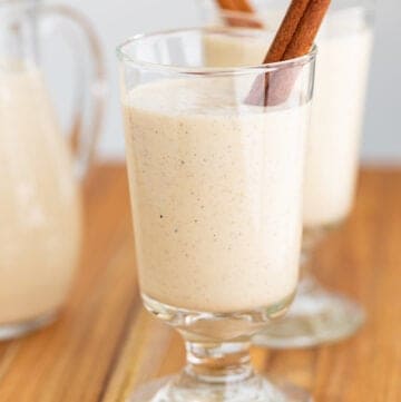 glass of eggnog with a cinnamon stick on a wooden surface