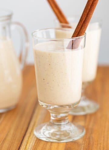 glass of eggnog with a cinnamon stick on a wooden surface