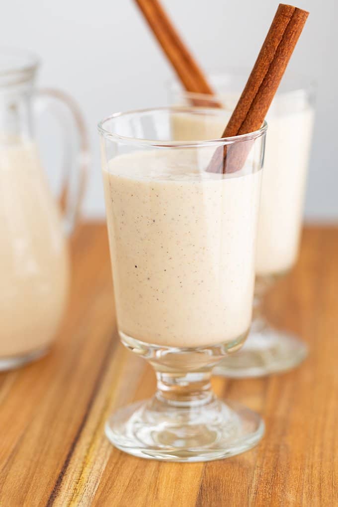 glass of eggnog with a cinnamon stick on a wooden surface