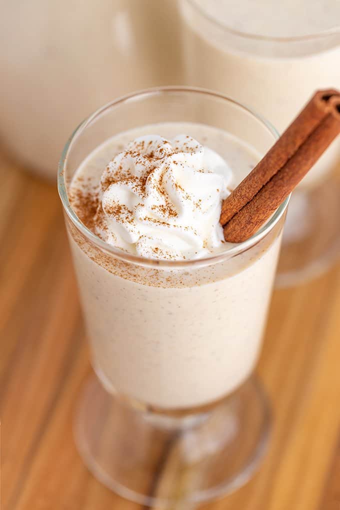 picture showing the cinnamon dusted whipped cream on top of the eggnog on a wood surface