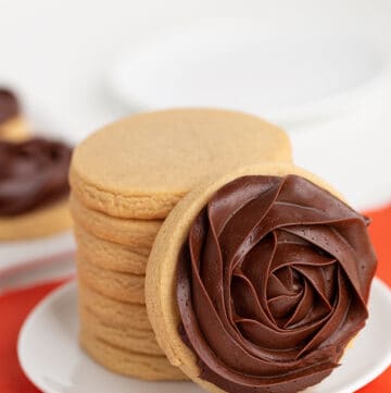 small white plate with a stack of cookies on it and a chocolate frosted cookie leaned against the stack