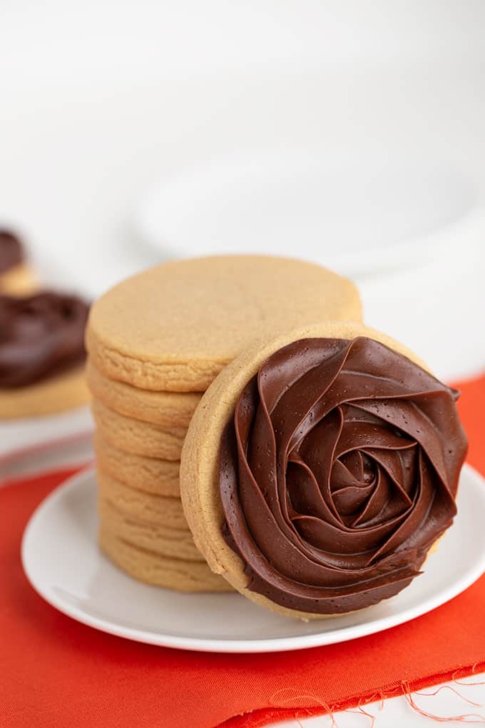 small white plate with a stack of cookies on it and a chocolate frosted cookie leaned against the stack