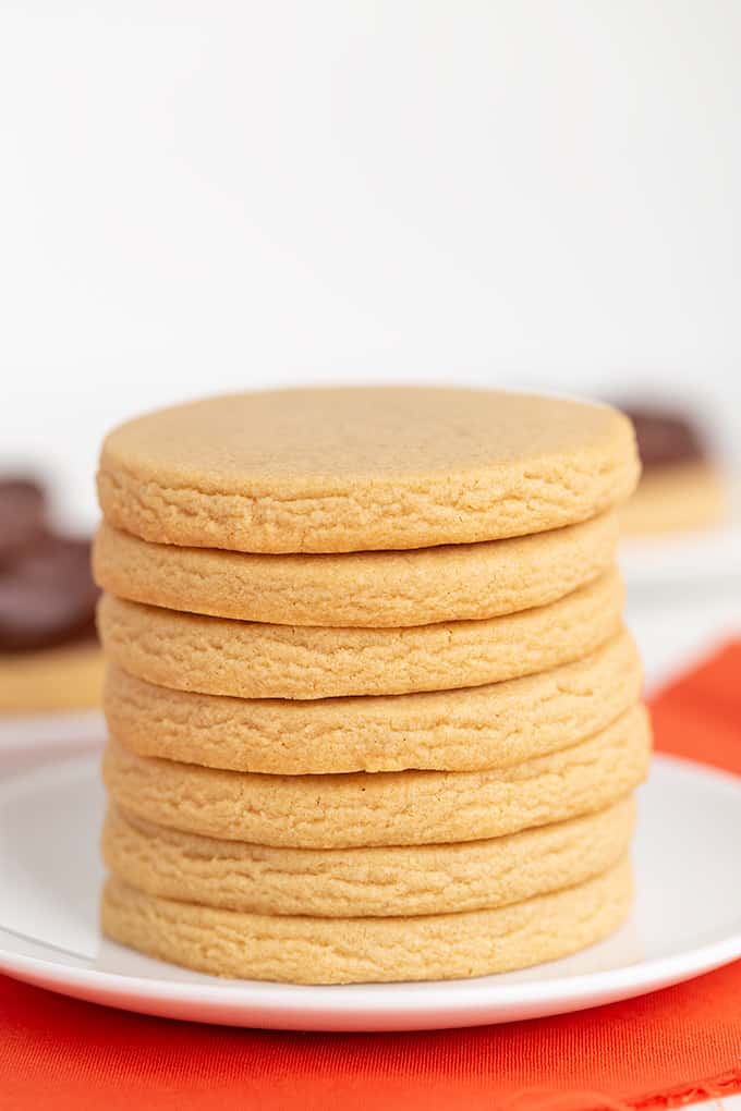 stack of cutout peanut butter cookies on a white plate with an orange linen