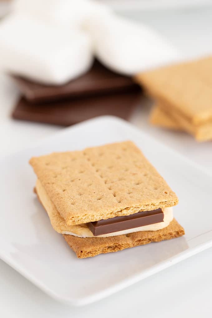 single s'more on a white square plate with ingredients behind it