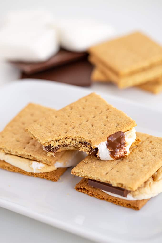 stack of s'mores on a white platter with a bite taken out of the top s'more