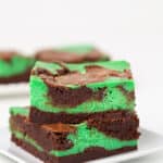 mint cheesecake brownies on a white surface with a small white plate