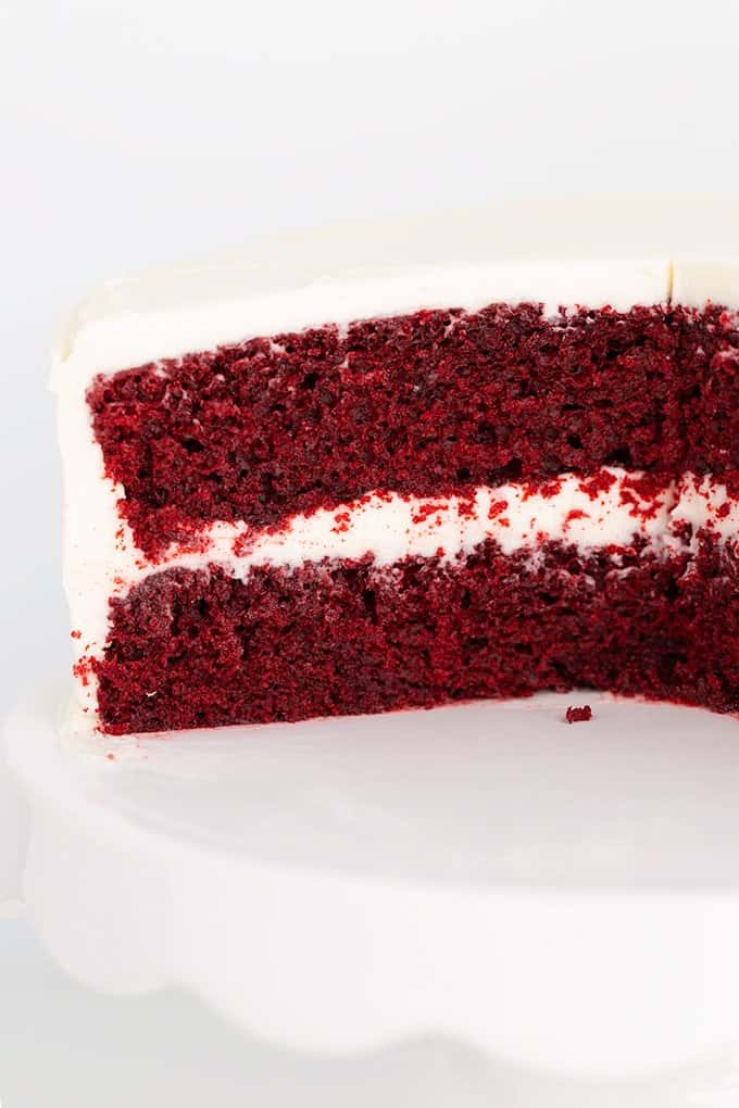 white cake plate with a red velvet layer cake on it with slices taken out