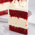 close up of a slice of cheesecake cake showing the layers of cake and cheesecake on a large white plate with the rest of the cake behind it