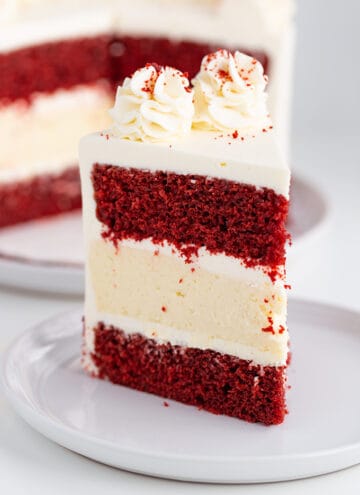 close up of a slice of cheesecake cake showing the layers of cake and cheesecake on a large white plate with the rest of the cake behind it