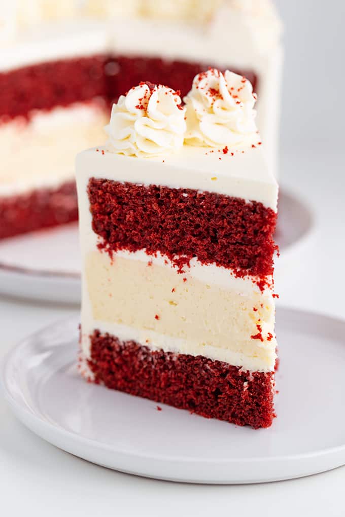 close up of a slice of cheesecake cake showing the layers of cake and cheesecake on a large white plate with the rest of the cake behind it