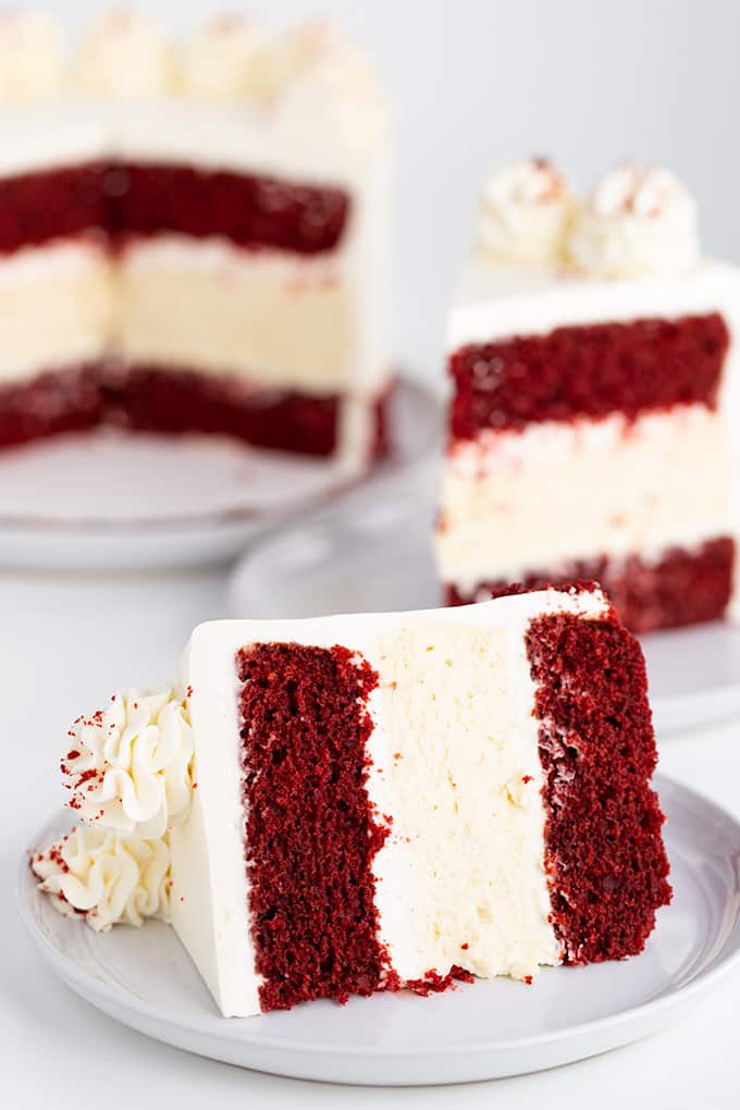 slice of cheesecake cake on its side on a white plate with a slice and the remaining cake behind it on a white surface
