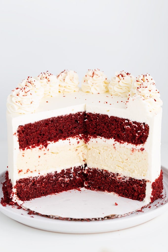 cheesecake cake with slices removed showing the inside of the cake on a cake board and white plate on a white surface