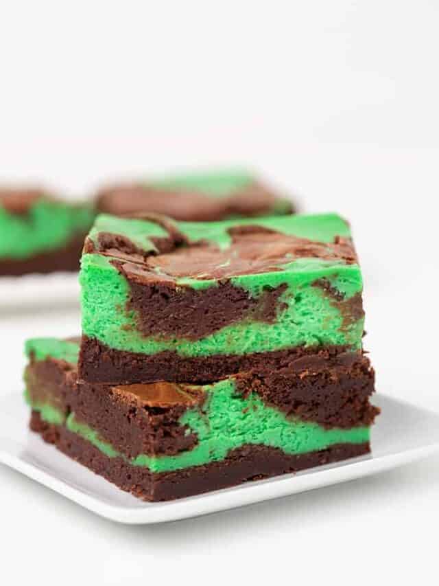 Two mint cheesecake brownies stacked on top of each other on a square white plate