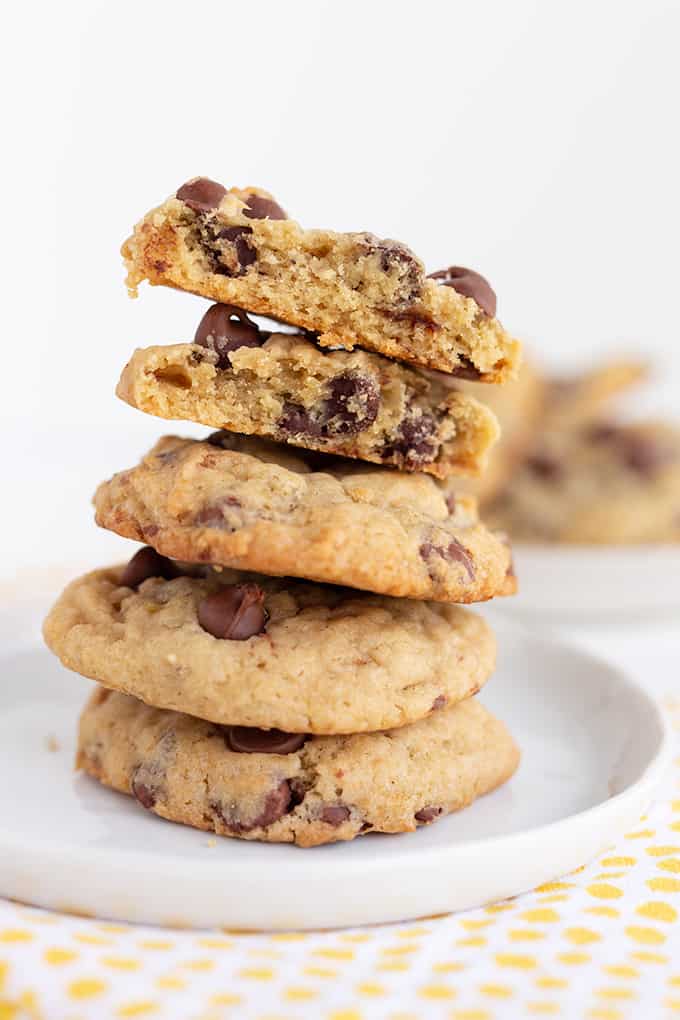 stack of banana choc chip cookies on a white plate with the top one broke in half on a white surface