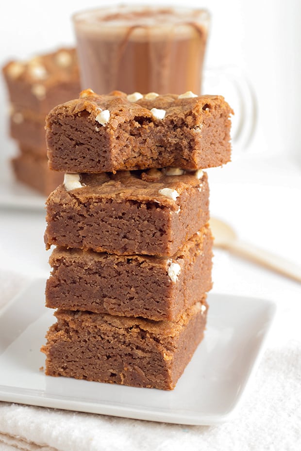 stack of brownies on a white square plate with a bite taken out of the top one on a white surface