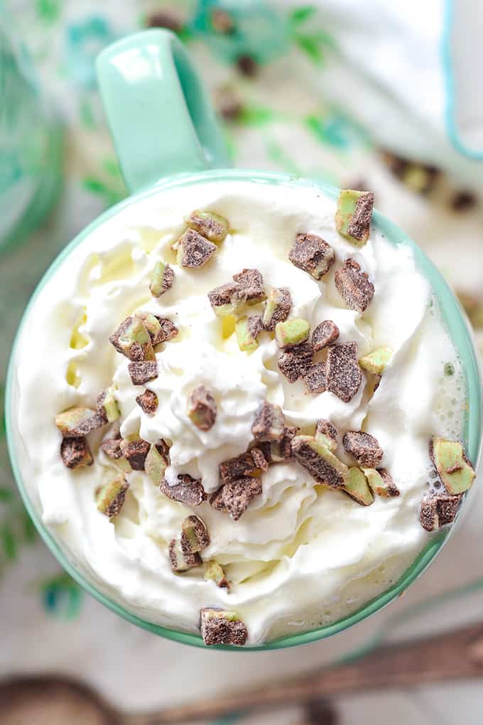 close up overhead image of white hot chocolate in a mug with whipped cream and mint pieces sprinkled on top
