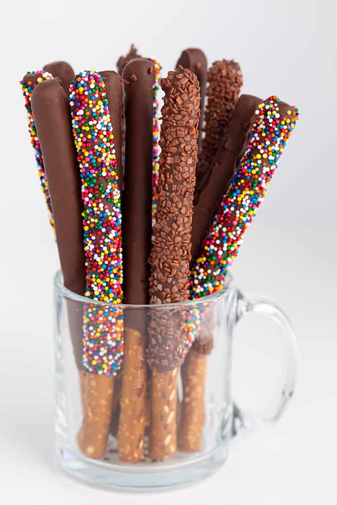 glass mug full of chocolate covered pretzel rods on a white surface