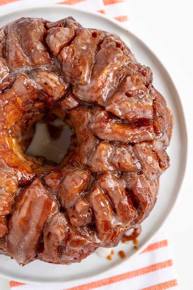 overhead image of an iced cinnamon roll monkey bread on a white plate on a white surface with a white and orange striped linen