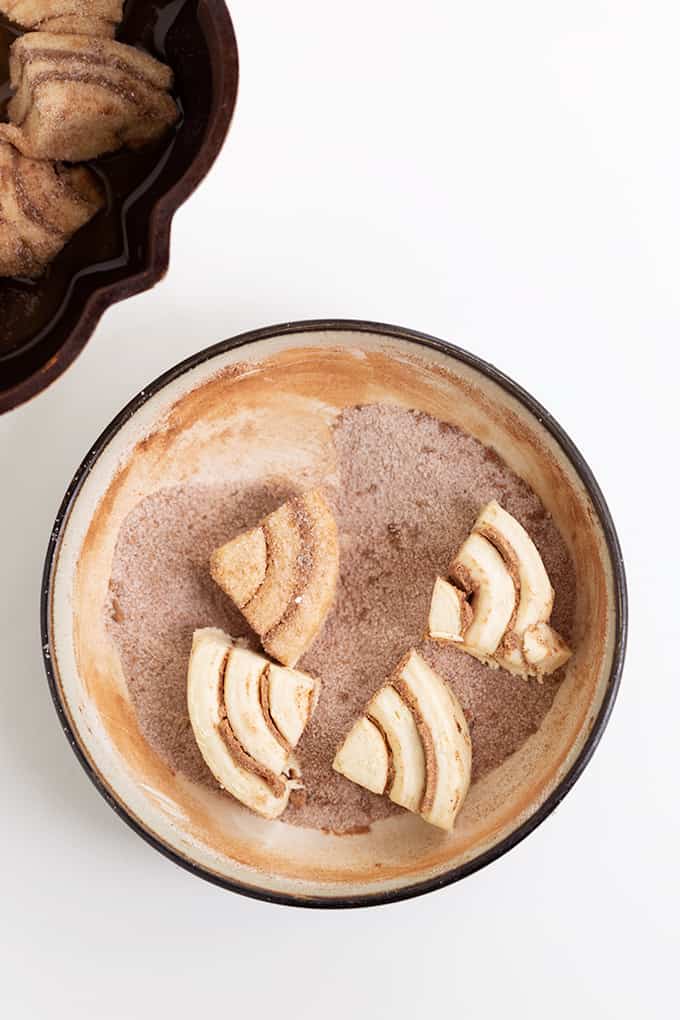 cinnamon roll in a bowl of cinnamon and sugar on a white surface