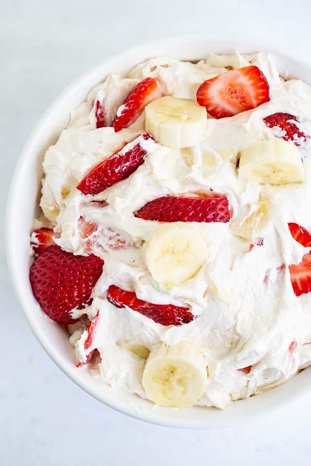 overhead photo of a bowl of strawberry banana cheesecake salad on a white surface