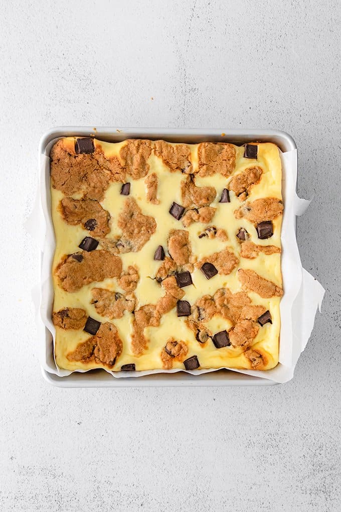 baked cookie cheesecake bars in a square pan on a white surface