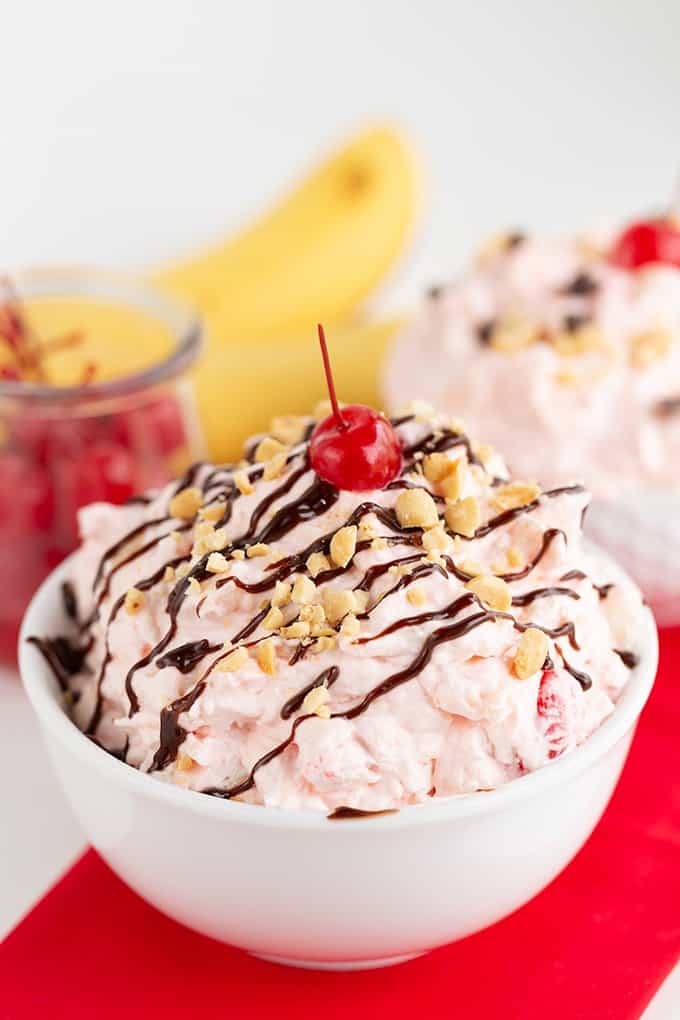 bowl of banana split fluff on a red linen with bananas and cherries behind it