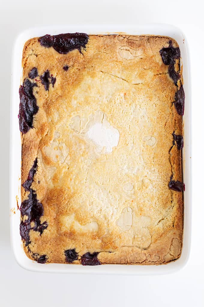 overhead photo of the blueberry lemon dump cake in a white baking dish on a white tabletop