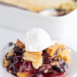 Side view of single serving of lemon blueberry dump cake in focus in front of a blurry full cake.
