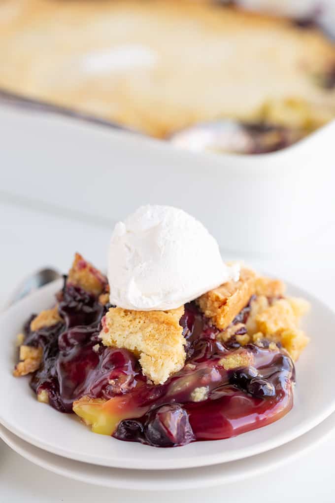 Side view of single serving of lemon blueberry dump cake in focus in front of a blurry full cake.