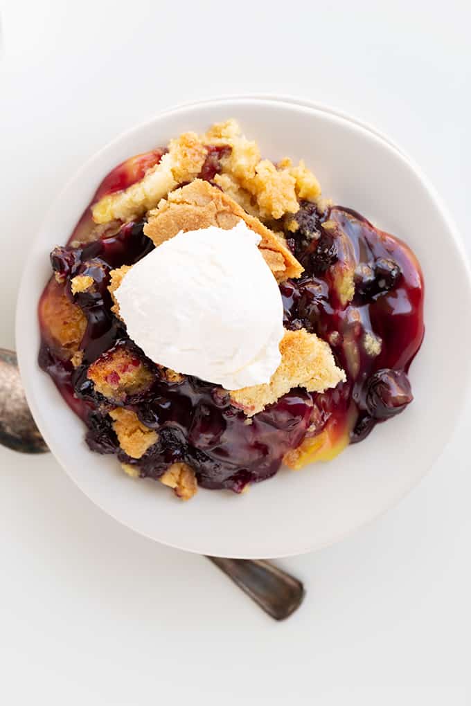 overhead photo of lemon blueberry dump cake on a small white plate with whipped topping on top and a spoon under the edge of plate