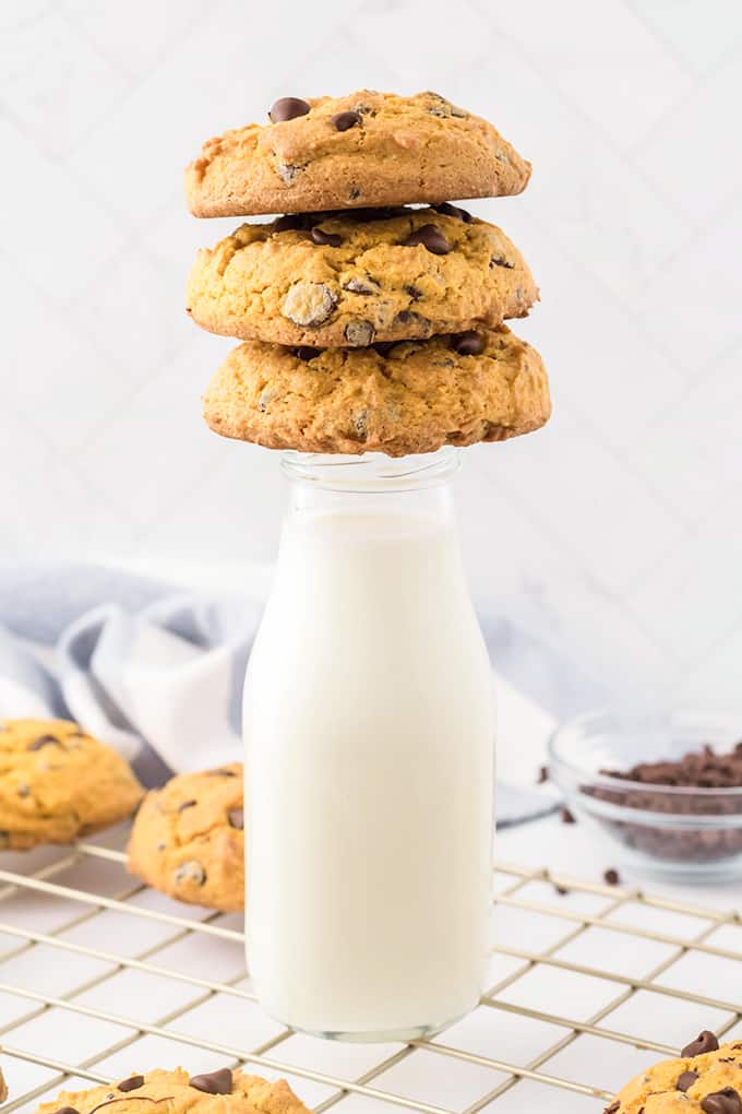 Three cream cheese chocolate chip cookies stacked on a milk jar.
