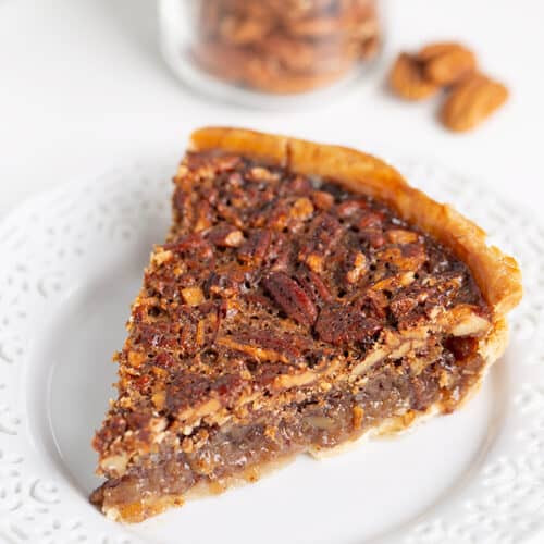 slice of pie showing the crispy top and some of the custard on a white plate with pecans behind it