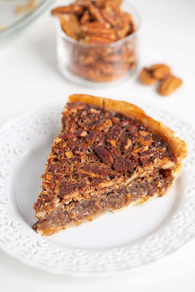 slice of pie showing the crispy top and some of the custard on a white plate with pecans behind it
