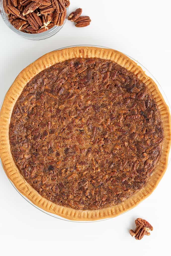 whole classic pecan pie with pecans scattered on the white surface