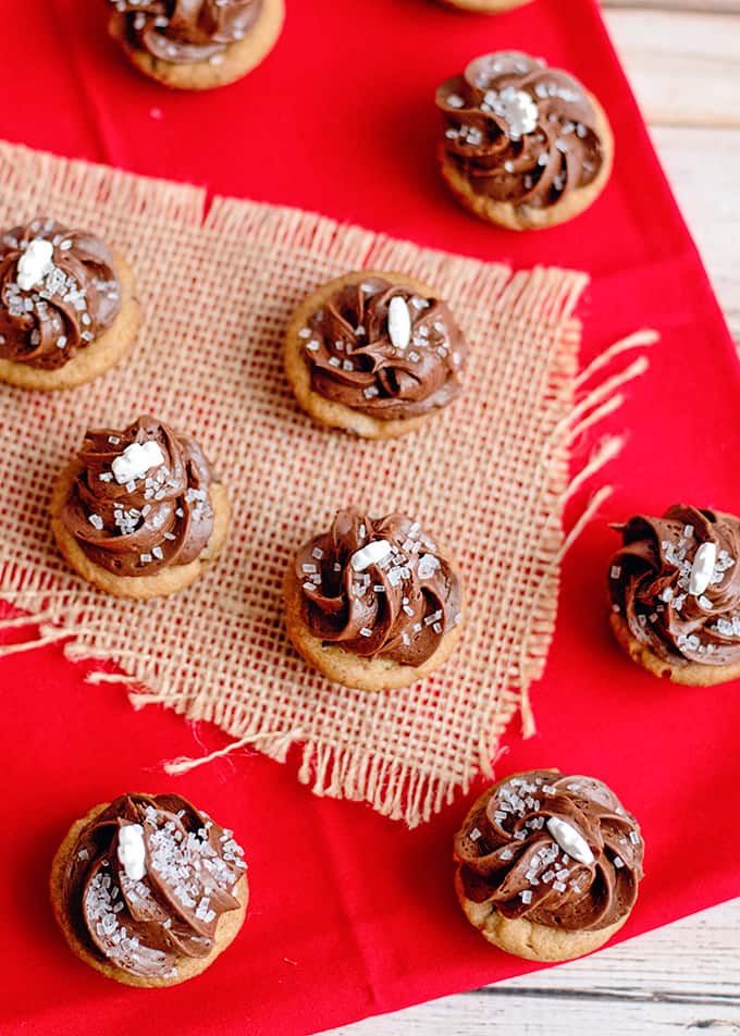 showing bite sized chocolate chip cookie cups with chocolate frosting on burlap, red linen, and a white surface