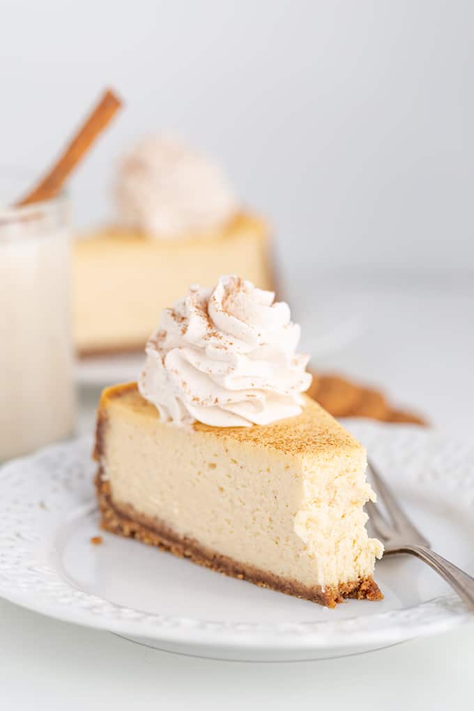 bite taken out of a cheesecake on a white plate with a fork next to the cheesecake on a white background