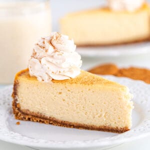 A slice of eggnog cheesecake on a plate next to a glass of milk.
