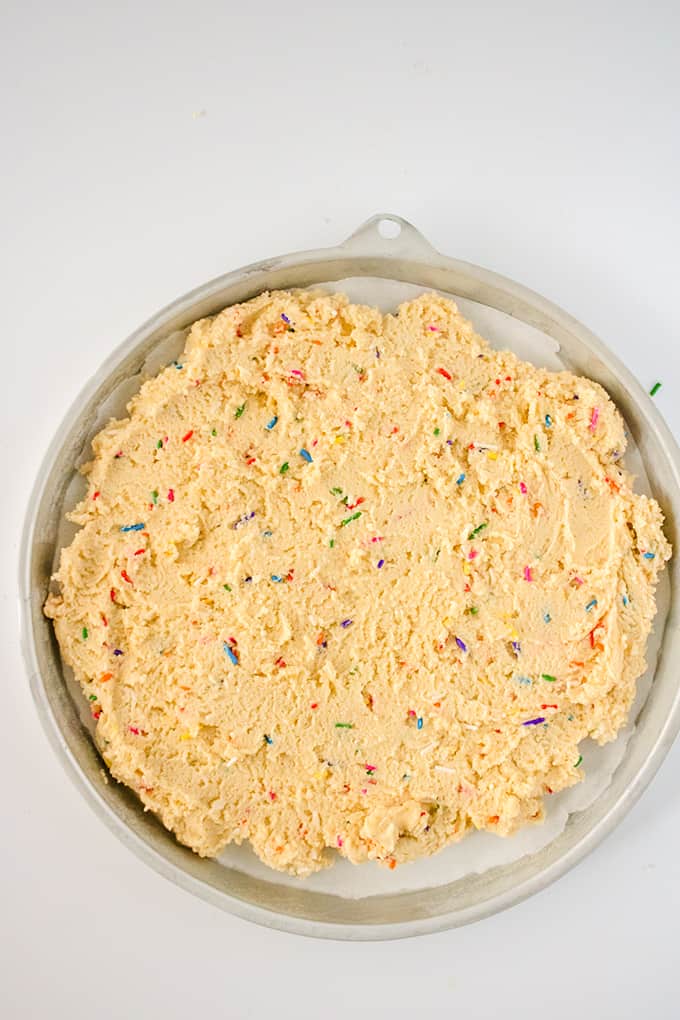 raw cookie dough in a cake pan on a white surface