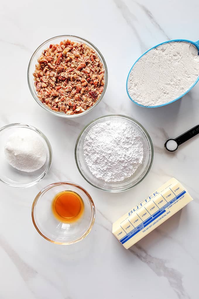 ingredients in glass bowls for pecan snowball cookies on a marble surface