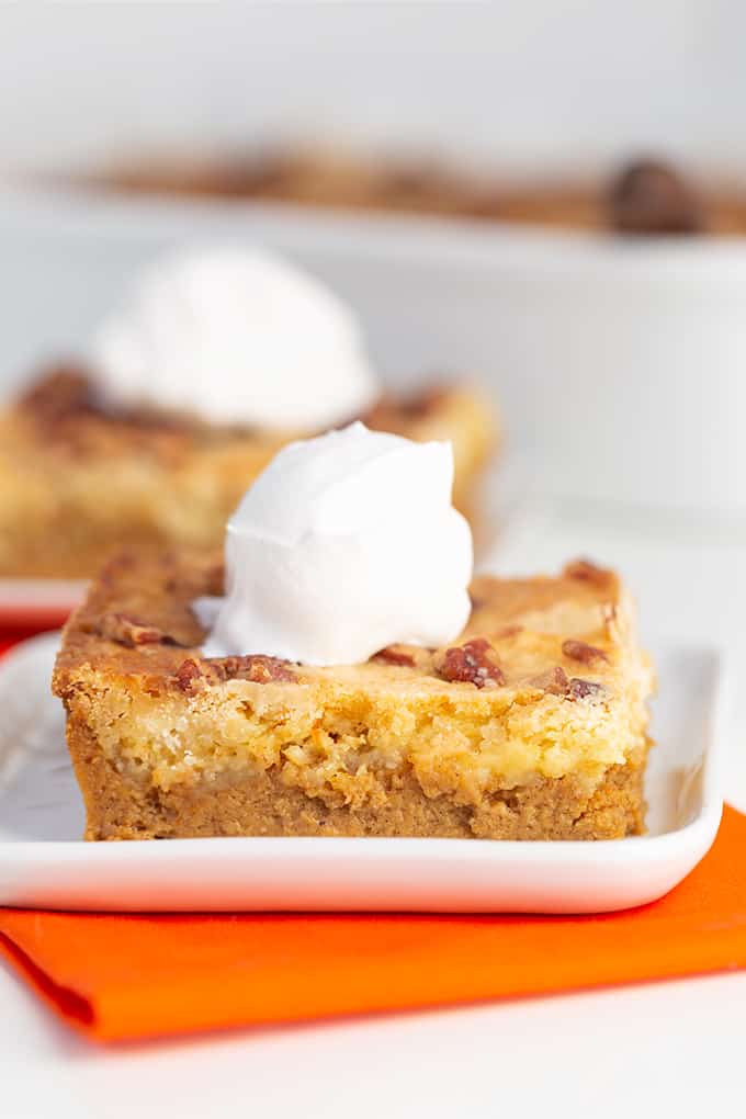 pumpkin bars on a square white plate with whipped cream on top and an orange linen under the plate