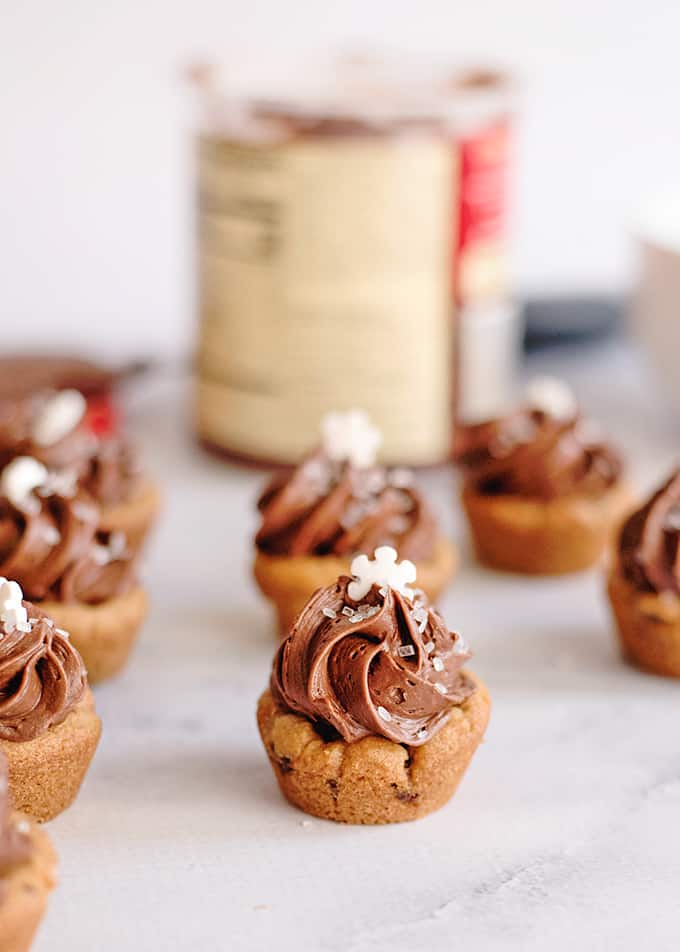 caramel chocolate chip cookie cups on a marbled surface with a jar of frosting behind it