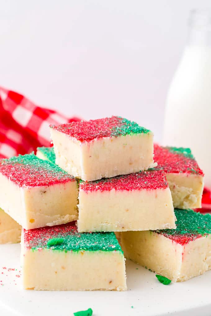 sugar cookie fudge stacked on a white surface with milk in a glass behind it