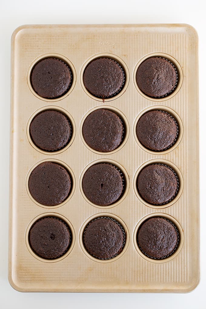 chocolate cupcakes in a gold cupcake pan on a white surface