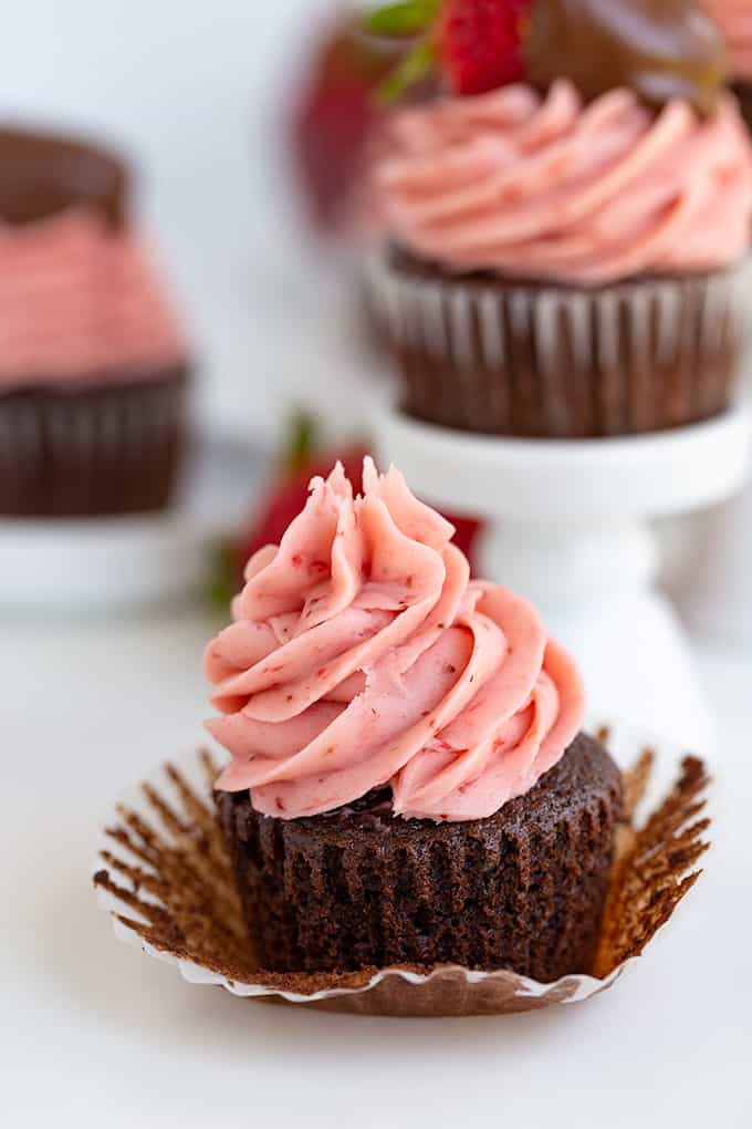 chocolate cupcakes with the paper liners peeled back with a tall swirl of fresh strawberry frosting on top