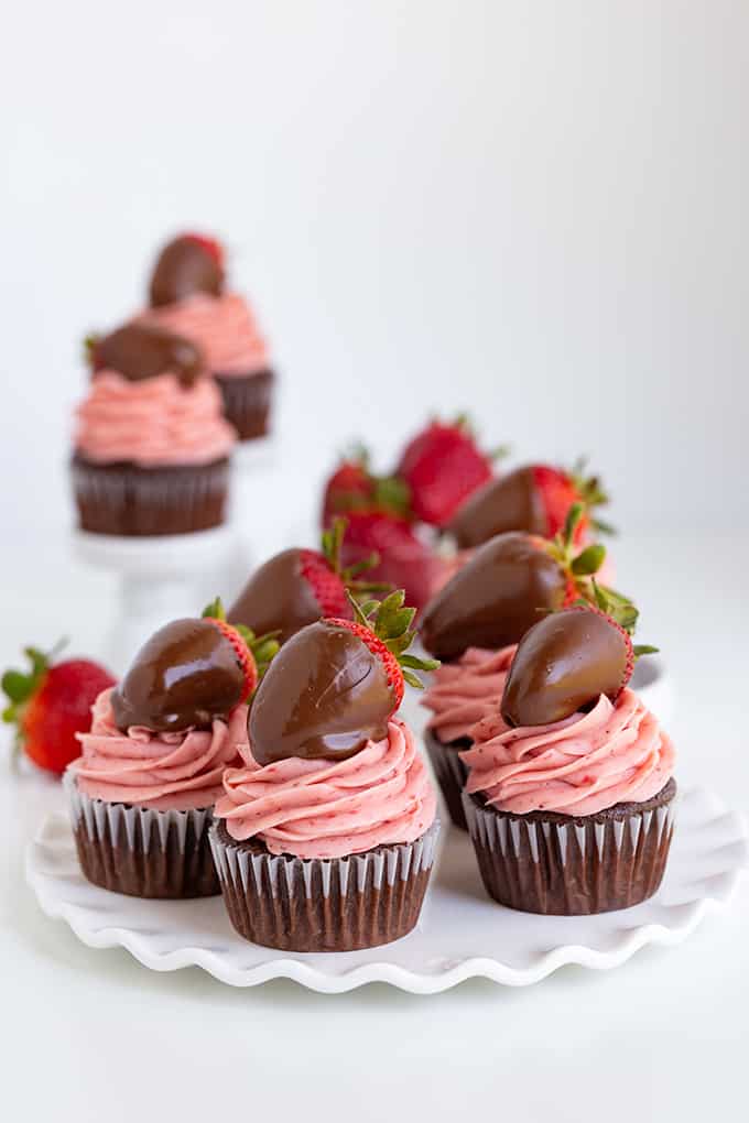 chocolate cupcakes with strawberry frosting on a white ruffled plate with two cupcakes behind it on cupcake stands