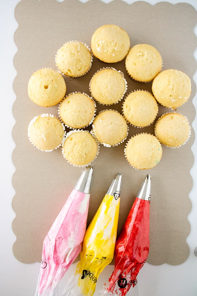 Undecorated cupcakes and frosting in piping bags.