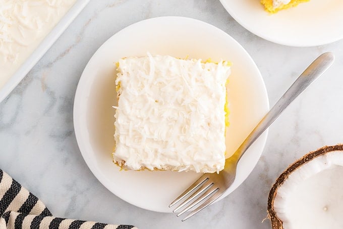 top down view of a single slice of pineapple coconut cake on white plate with fork and a marble slab background