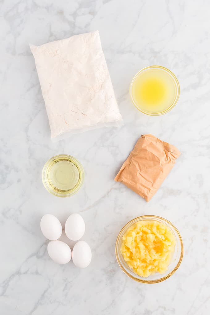 Ingredients: cake mix, eggs, oil, crushed pineapple, pineapple juice, and vanilla pudding mix overhead photo layed out on a marble slab
